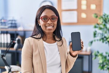 Wall Mural - African young woman holding smartphone showing blank screen looking positive and happy standing and smiling with a confident smile showing teeth