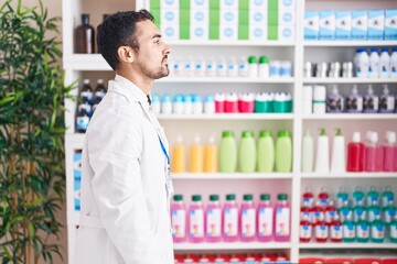 Sticker - Handsome hispanic man working at pharmacy drugstore looking to side, relax profile pose with natural face and confident smile.