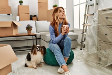 Wall Mural - Young caucasian woman drinking coffee sitting with dog at new home