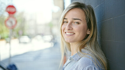 Wall Mural - Young blonde woman smiling confident standing at street