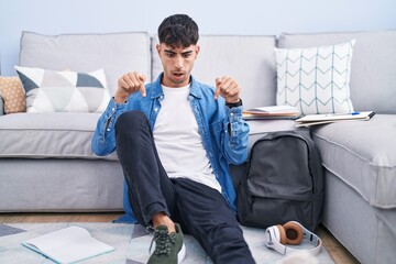 Wall Mural - Young hispanic man sitting on the floor studying for university pointing down with fingers showing advertisement, surprised face and open mouth