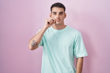 Poster - Handsome hispanic man standing over pink background mouth and lips shut as zip with fingers. secret and silent, taboo talking