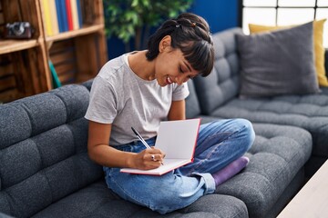 Canvas Print - Young woman writing on book sitting on sofa at home