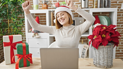 Wall Mural - Young blonde woman shopping with laptop and credit card celebrating christmas with winner expression at dinning room