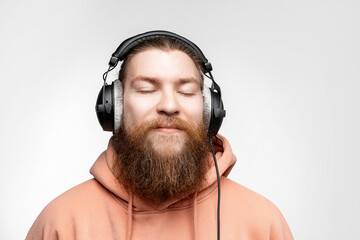 Wall Mural - Scandinavian handsome contented man closed his eyes and listens to music in professional headphones isolated on gray background. Happy guy with ginger hairstyle and beard. Modern digital technologies