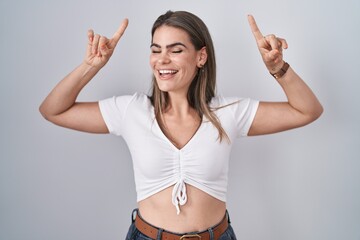 Canvas Print - Young beautiful woman wearing casual white t shirt smiling amazed and surprised and pointing up with fingers and raised arms.