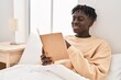 © Krakenimages.com - African american man reading book sitting on bed at bedroom