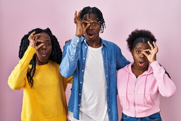 Poster - Group of three young black people standing together over pink background doing ok gesture shocked with surprised face, eye looking through fingers. unbelieving expression.