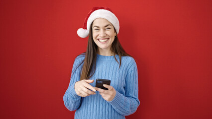 Sticker - Young caucasian woman wearing christmas hat using smartphone over isolated red background