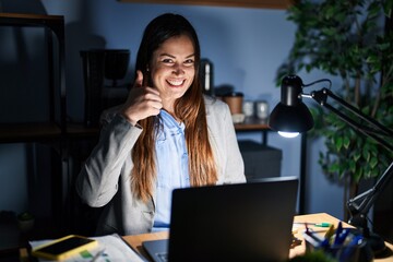 Sticker - Young brunette woman working at the office at night doing happy thumbs up gesture with hand. approving expression looking at the camera showing success.