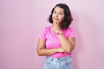 Canvas Print - Young hispanic woman standing over pink background looking confident at the camera smiling with crossed arms and hand raised on chin. thinking positive.