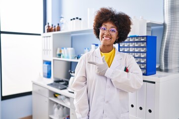 Sticker - Young african american woman working at scientist laboratory smiling cheerful pointing with hand and finger up to the side