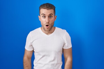 Poster - Young caucasian man standing over blue background afraid and shocked with surprise and amazed expression, fear and excited face.