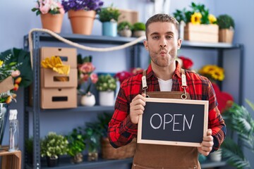 Sticker - Young caucasian man working at florist holding open sign making fish face with mouth and squinting eyes, crazy and comical.