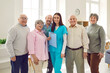 Portrait of friendly female nurse, caregiver or psychologist woman standing with a group of senior people and looking cheerful at camera. Psychological support in nursing home for retirement.