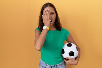 Canvas Print - Young hispanic woman holding ball yawning tired covering half face, eye and mouth with hand. face hurts in pain.