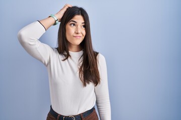 Sticker - Young brunette woman standing over blue background confuse and wondering about question. uncertain with doubt, thinking with hand on head. pensive concept.