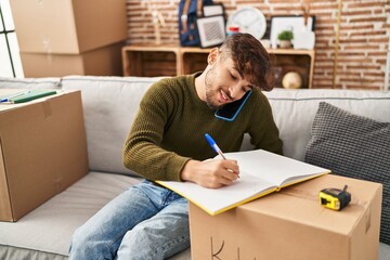 Sticker - Young arab man talking on smartphone writing on notebook at new home