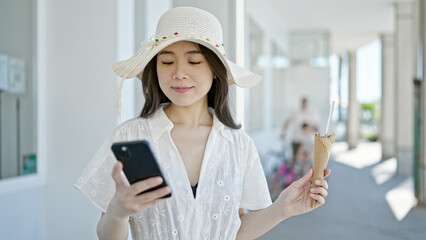 Wall Mural - Young chinese woman tourist eating ice cream using smartphone at street