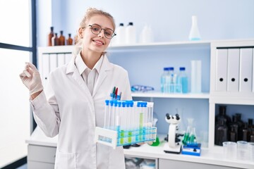 Sticker - Young caucasian woman working at scientist laboratory holding samples smiling happy pointing with hand and finger to the side