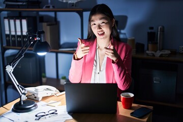 Wall Mural - Chinese young woman working at the office at night pointing fingers to camera with happy and funny face. good energy and vibes.