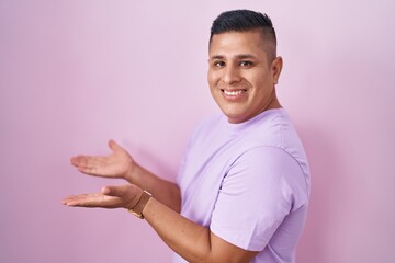 Sticker - Young hispanic man standing over pink background pointing aside with hands open palms showing copy space, presenting advertisement smiling excited happy