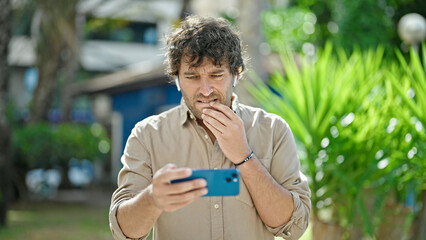 Wall Mural - Young hispanic man watching video on smartphone concentrated at park