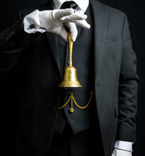 Portrait Of Butler Or Hotel Concierge In Dark Suit And White Gloves Holding Gold Bell. Concept Of Ring For Service And Professional Hospitality.
