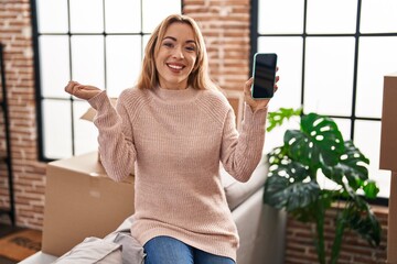 Canvas Print - Hispanic woman moving to a new home showing smartphone screen screaming proud, celebrating victory and success very excited with raised arm