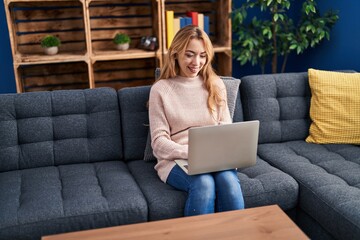 Poster - Young woman using laptop sitting on sofa at home