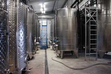 silver metal reservoir tanks for the fermentation of wine with ladder and hose in shot