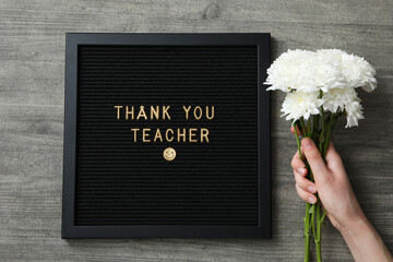 Wall Mural - Black frame with text, flowers in female hand on wooden background