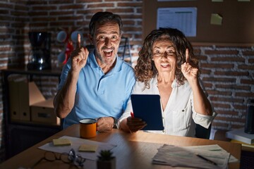 Poster - Middle age hispanic couple using touchpad sitting on the table at night pointing finger up with successful idea. exited and happy. number one.