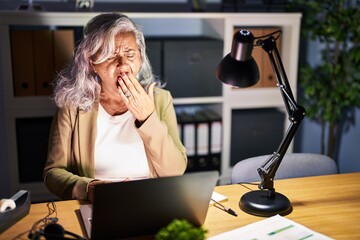 Sticker - Middle age woman with grey hair working using computer laptop late at night bored yawning tired covering mouth with hand. restless and sleepiness.