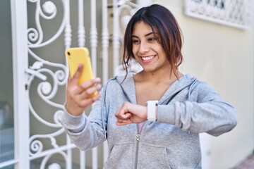 Poster - Young hispanic woman wearing sportswear looking stopwatch using smartphone at street