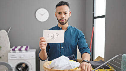 Wall Mural - Young hispanic man holding basket with clothes asking for help at laundry room