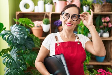 Wall Mural - Young beautiful hispanic woman florist smiling confident holding binder at flower shop