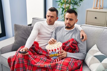 Canvas Print - Homosexual couple eating popcorn watching tv skeptic and nervous, frowning upset because of problem. negative person.