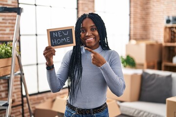 Sticker - African american woman holding blackboard with new home text smiling happy pointing with hand and finger