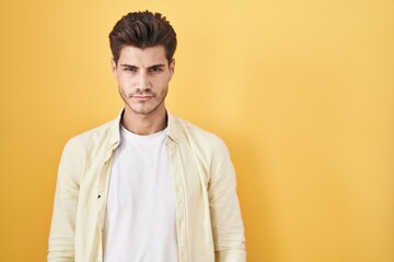 Wall Mural - Young hispanic man standing over yellow background skeptic and nervous, frowning upset because of problem. negative person.