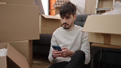 Sticker - Young hispanic man using smartphone sitting on floor at new home