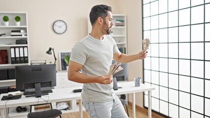 Wall Mural - Young hispanic man business worker holding dollars dancing at office