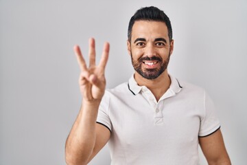 Canvas Print - Young hispanic man with beard wearing casual clothes over white background showing and pointing up with fingers number three while smiling confident and happy.