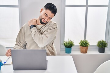 Wall Mural - Young arab man suffering for back ache sitting on table working at home