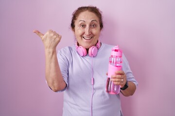 Poster - Senior woman wearing sportswear and headphones pointing to the back behind with hand and thumbs up, smiling confident