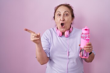 Poster - Senior woman wearing sportswear and headphones surprised pointing with finger to the side, open mouth amazed expression.