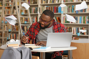 Wall Mural - African-American student preparing for exam in library with flying books