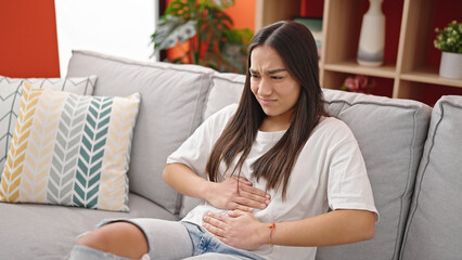 Canvas Print - Young beautiful hispanic woman suffering for stomach ache sitting on sofa at home