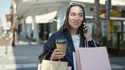 Sticker - Young beautiful hispanic woman talking on smartphone holding shopping bags and coffee at coffee shop terrace