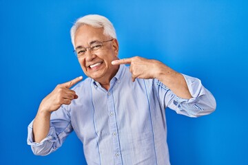 Poster - Hispanic senior man wearing glasses smiling cheerful showing and pointing with fingers teeth and mouth. dental health concept.